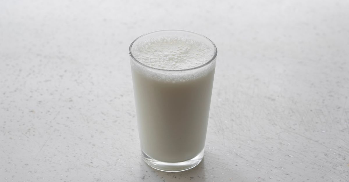 A frothy glass of milk on a textured white surface, captured with minimalism.